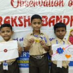 Three boys in school uniforms pose in front of a banner each holding a handmade craft cardsouvenir